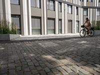 a man riding a bicycle past an office building with an outside courtyard on a sunny day