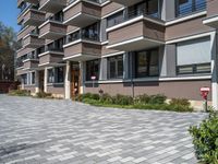 the apartment complex has large stones on the pavement and green plants growing by the building entrance