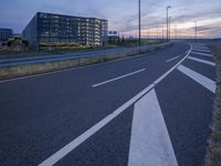 an empty road that is at dusk near the building in the distance and there are some traffic lights