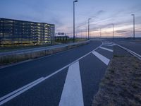 an empty road that is at dusk near the building in the distance and there are some traffic lights