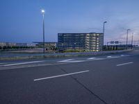 an empty road that is at dusk near the building in the distance and there are some traffic lights