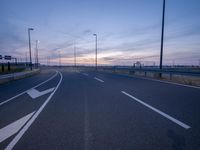 an empty road that is at dusk near the building in the distance and there are some traffic lights