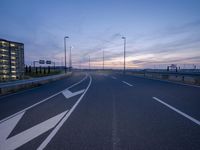 an empty road that is at dusk near the building in the distance and there are some traffic lights