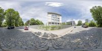 a fisheye lens shows a cobblestone street, cars on the left side