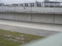 the man is riding his skateboard along a concrete bridge over a grassy area next to a building