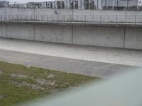 the man is riding his skateboard along a concrete bridge over a grassy area next to a building