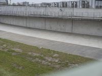 the man is riding his skateboard along a concrete bridge over a grassy area next to a building