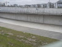 the man is riding his skateboard along a concrete bridge over a grassy area next to a building