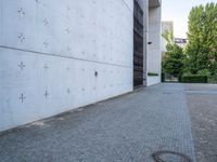 an empty paved area near a very large building with a small round metal door and two trees