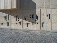 cobblestone driveway surrounded by modern buildings on sunny day with sun reflecting onto the windows