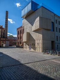 cobblestone driveway surrounded by modern buildings on sunny day with sun reflecting onto the windows