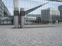 the building has three large posts in front of it on a cobble stone sidewalk