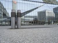 the building has three large posts in front of it on a cobble stone sidewalk