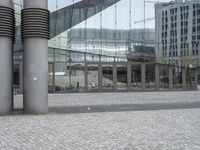 the building has three large posts in front of it on a cobble stone sidewalk