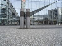 the building has three large posts in front of it on a cobble stone sidewalk