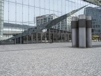 the building has three large posts in front of it on a cobble stone sidewalk