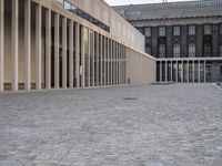 a person that is sitting down next to the sidewalk outside a building with glass walls