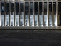 a man on a sidewalk standing in front of a building with some windows open at night