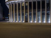 a man on a sidewalk standing in front of a building with some windows open at night