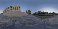 fish eye view of a circular stone area with some tall buildings in the background and trees around