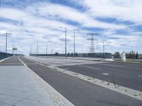 the highway is empty for traffic and has street lamps and tall poles on it and some blue sky