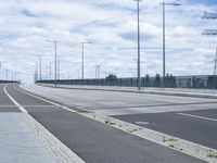 the highway is empty for traffic and has street lamps and tall poles on it and some blue sky