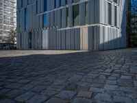 cobblestone driveway surrounded by modern buildings on sunny day with sun reflecting onto the windows