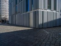 cobblestone driveway surrounded by modern buildings on sunny day with sun reflecting onto the windows