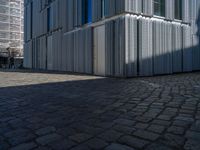 cobblestone driveway surrounded by modern buildings on sunny day with sun reflecting onto the windows