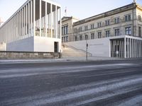 the large, empty sidewalk with multiple columns in front of the building with two signs