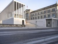 the large, empty sidewalk with multiple columns in front of the building with two signs