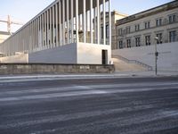 the large, empty sidewalk with multiple columns in front of the building with two signs