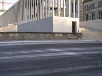 the large, empty sidewalk with multiple columns in front of the building with two signs