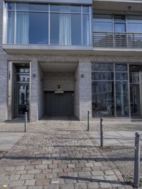the entrance to a very tall and modern building, on a brick sidewalk in front of a door on a street