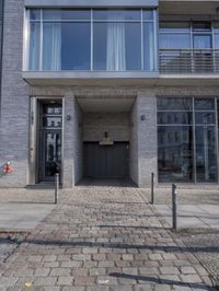 the entrance to a very tall and modern building, on a brick sidewalk in front of a door on a street