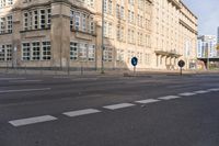 two signs on the corner of a deserted street in front of buildings and a sky