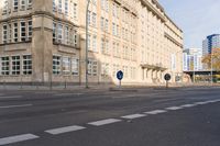 two signs on the corner of a deserted street in front of buildings and a sky