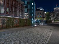 a street with buildings and lights on the side in the dark night time with a cobblestone road with cobblestones in front