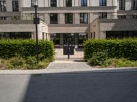 an entrance to a building with lots of trees and bushes in front of it on the ground