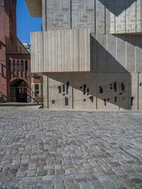 cobblestone driveway surrounded by modern buildings on sunny day with sun reflecting onto the windows