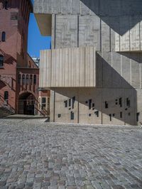 cobblestone driveway surrounded by modern buildings on sunny day with sun reflecting onto the windows