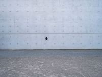 a white wall has a round window on it with two dark spots in the center