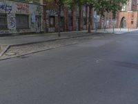 the person riding his skateboard down a quiet street in the daytime light and on the pavement there is graffiti