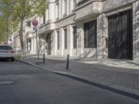 an empty sidewalk lined with buildings and a parked car behind it, in front of a sign saying do not enter