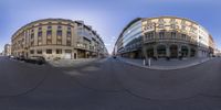 a 360 lens photo of two buildings in an intersection with cars and people passing each other on either side