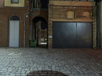 a large black door next to two doors on a brick building at night with one door open