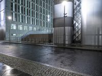 some buildings and some rain on the street near one another at night in a city