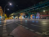 the empty street is filled with people walking and biking under an overpass at night