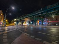 the empty street is filled with people walking and biking under an overpass at night