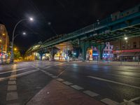 the empty street is filled with people walking and biking under an overpass at night